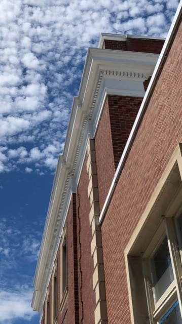 Image of an upward glance at a blue sky studded with small white clouds against which a gorgeous neo-classical cornice defines space.