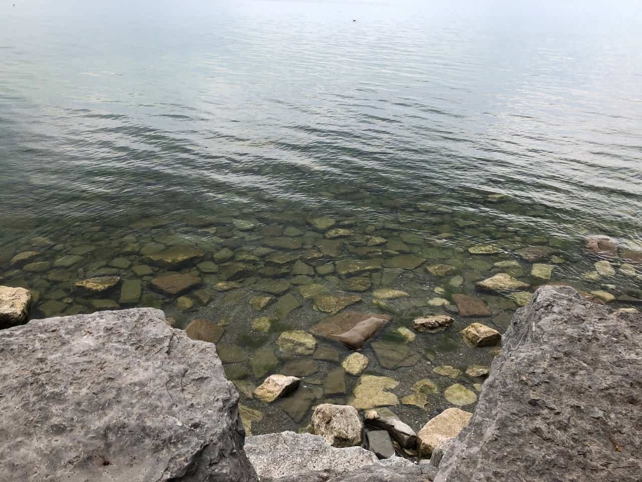 Image of large stones at the edge of Lake Ontario with smaller subsurface stone appearing through ripples on the surface, through sun and mist.