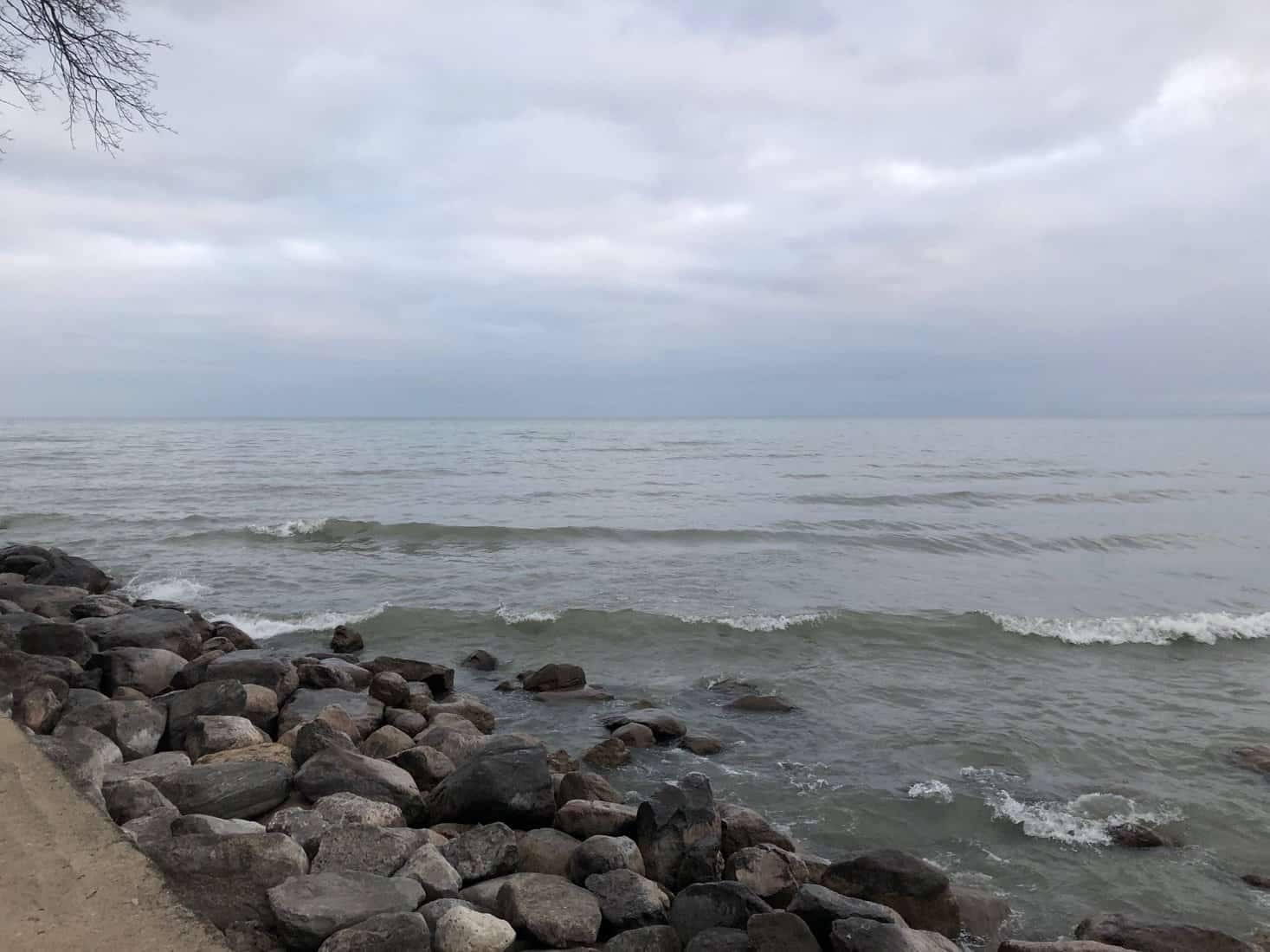 Waves of energy moving water across stones and into and along a breakwall, on a grey winter day at Oakville, Ontario.