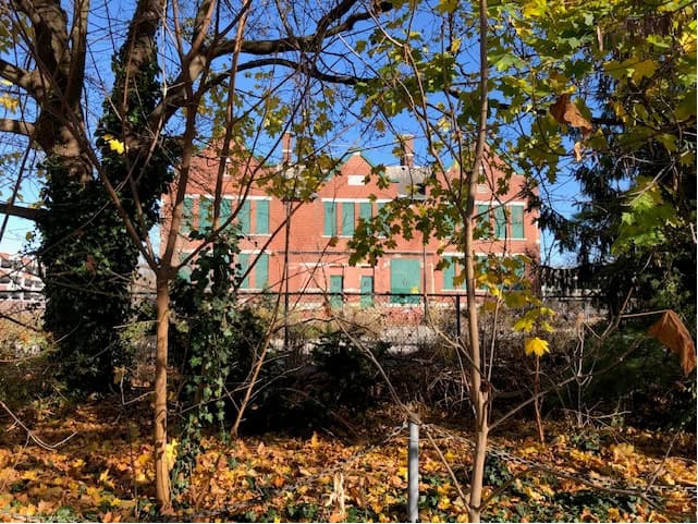 Boarded-up brick building with three gable ends facing Reynolds St., Oakville. Seen through trees.