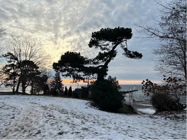 Late December view of Oakville harbour from Erchless Estate. Emerging light scattering clouds in yellow-blue-orange sky over blue lake from snow-clad hill.